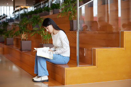 坐在图书馆台阶上看书的女学生高清图片