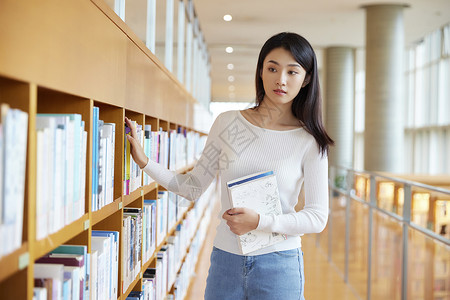 青少前女学生女学生在图书馆书架前挑选书籍背景