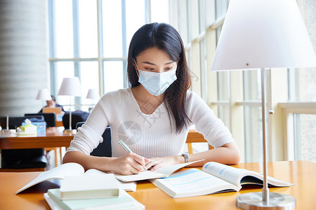 戴口罩的女学生在自习室学习背景图片