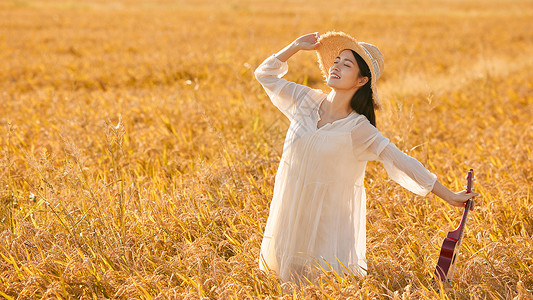 手拿尤克里里走在稻田的年轻女性高清图片