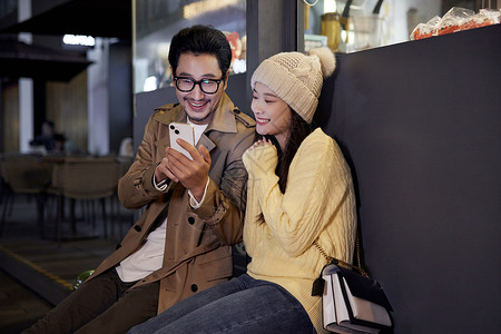 青年男女冬日夜晚街边休息玩手机图片