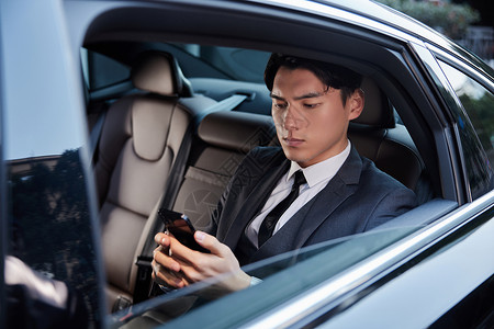 穿西装的年轻老板坐在轿车里使用手机高清图片