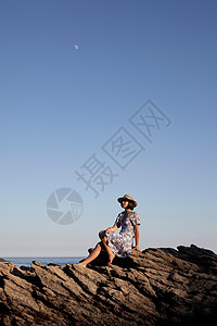 坐在海边岩石上的女孩图片