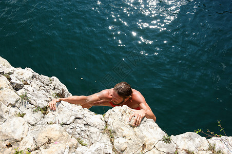 男人攀爬陡峭的岩石面图片