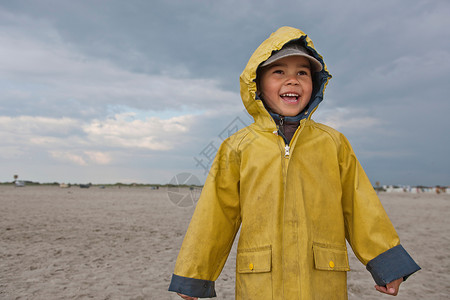 微笑的男孩在海滩上穿着雨衣图片