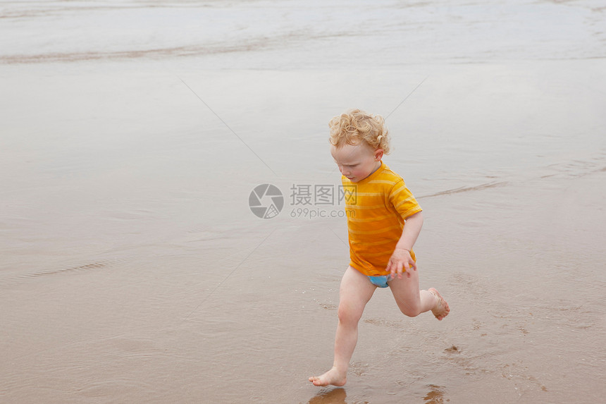 男孩在海滩的沙滩上奔跑图片