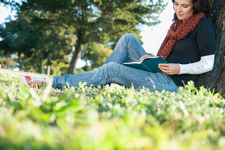 靠在草地上阅读书籍的女性图片