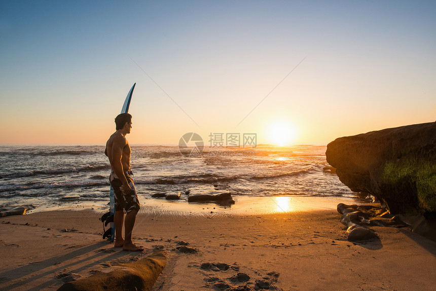 男子在岩石海滩上携带冲浪板图片