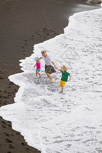 中期成年妇女母亲和儿童在海浪中行走背景