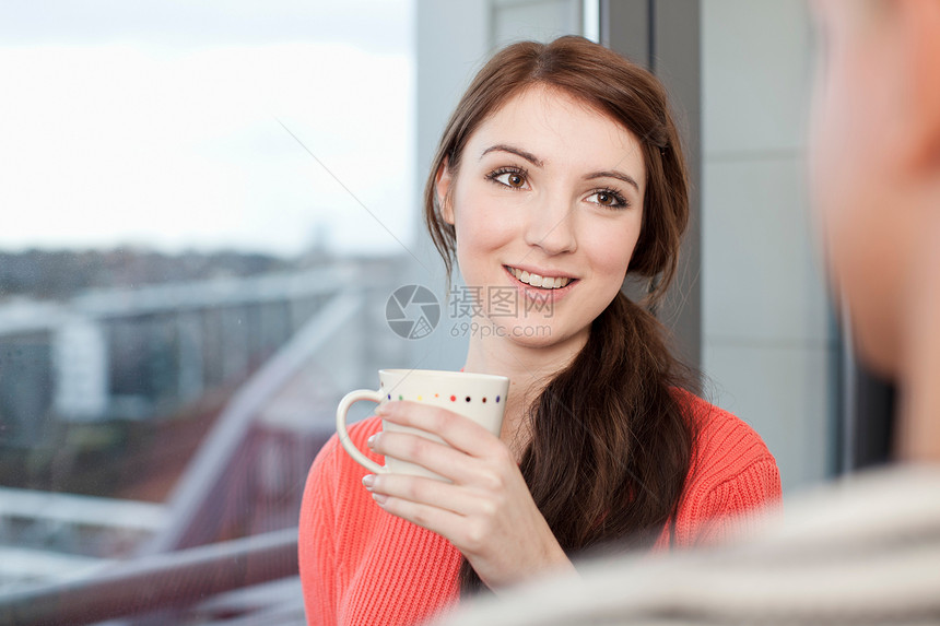 女青年手拿咖啡靠在窗边图片