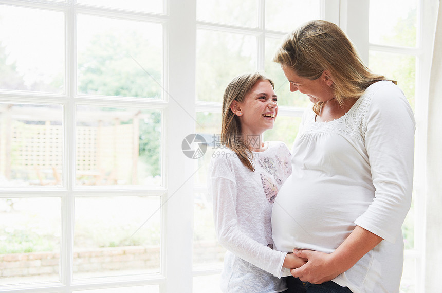 怀孕母亲与女儿在窗边微笑对视图片