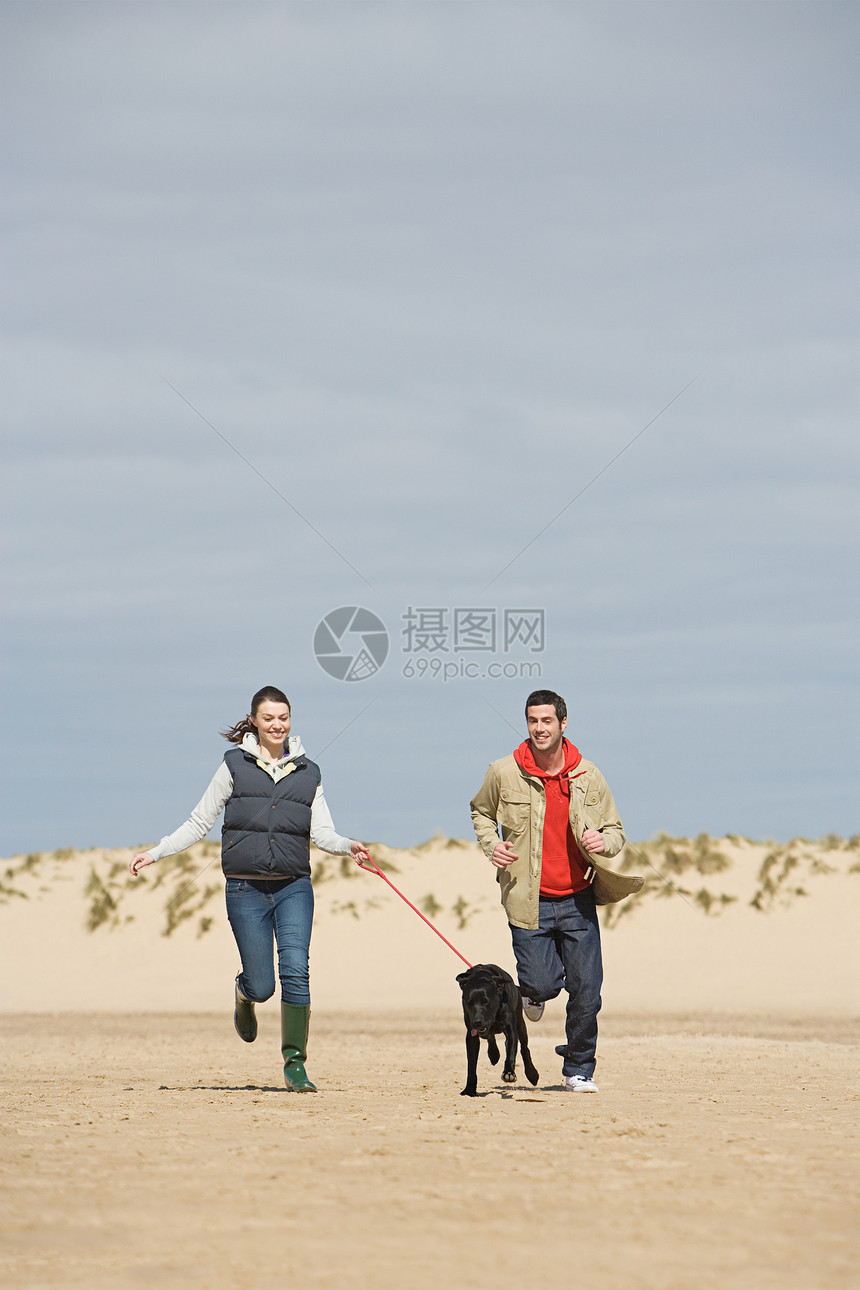 夫妇在海滩上牵着狗一起奔跑图片