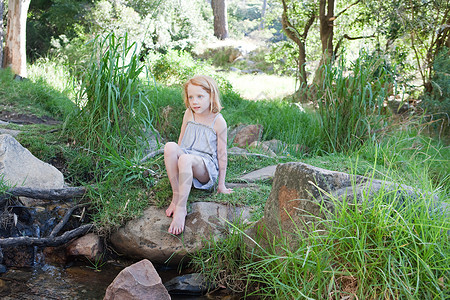 女孩坐在河边岩石上图片