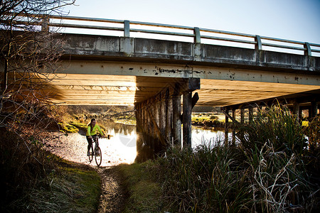 在桥下骑着自行车的妇女图片