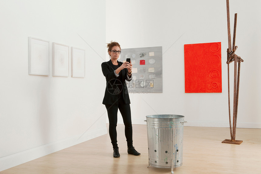 年轻美女使用手机在画廊拍摄艺术作品图片