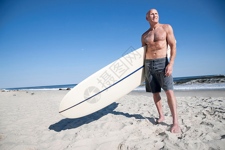 站在海滩上手拿冲浪板的男人图片
