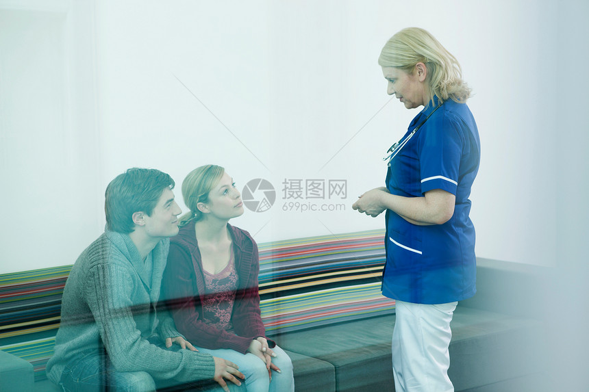 在医院等候室与护士交流的年轻夫妇图片