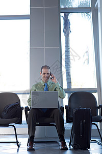 坐在椅子上腿上放着笔记本电脑的男人在打电话图片