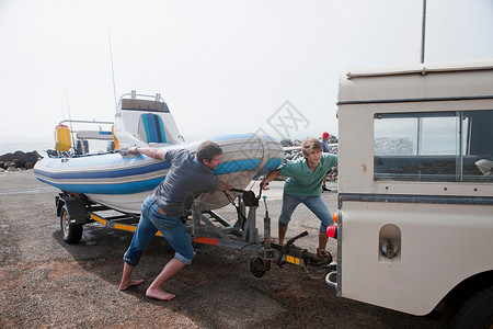 两名青年男子将小船拖上修理车图片