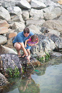 父亲和女儿站在河边的岩石上捕鱼图片
