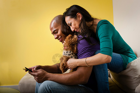 成年中夫妇与狗坐在沙发上玩手机图片