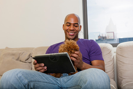 成年男子坐在沙发上抱着狗看平板电脑图片