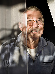 戴眼镜的中年男子在阳光窗帘下微笑背景图片