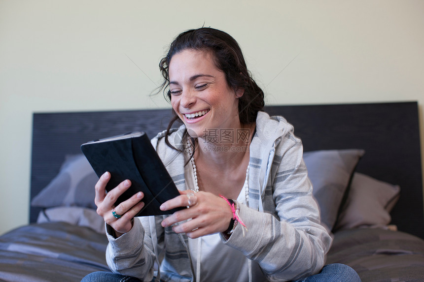 坐在床上的年轻妇女开心的玩平板电脑图片