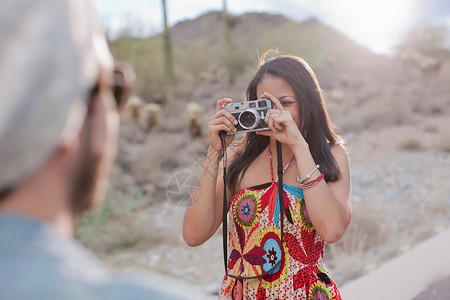 在沙漠路上拍摄男友的年轻女子图片