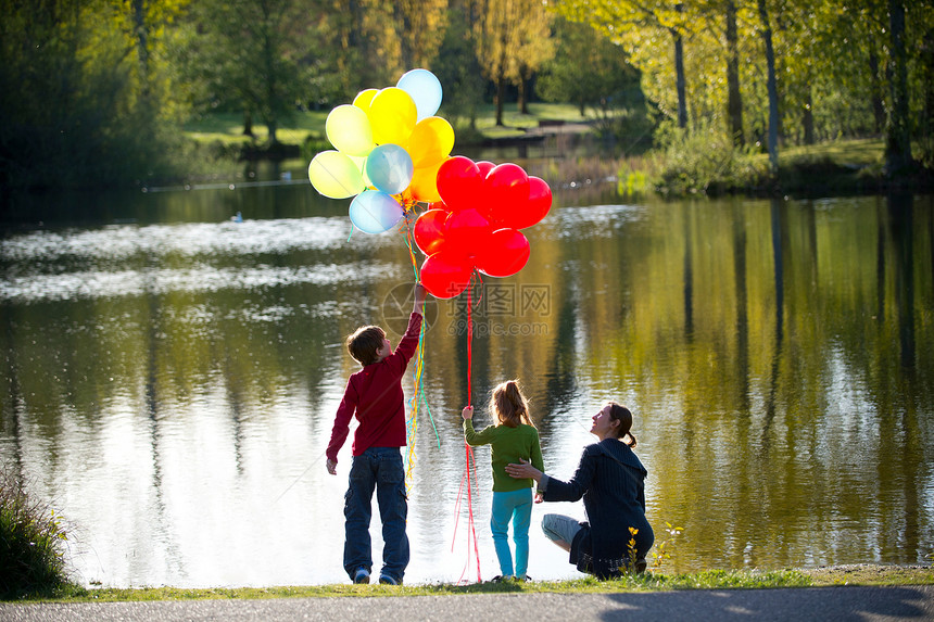 母亲和孩子在湖前带着一堆气球图片
