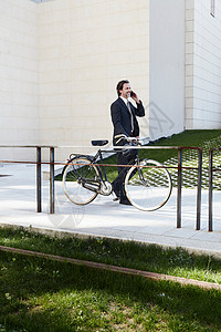 扶着自行车使用移动电话的中年商人图片