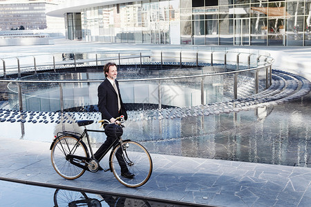 城市中扶着自行车行走的商务男性图片