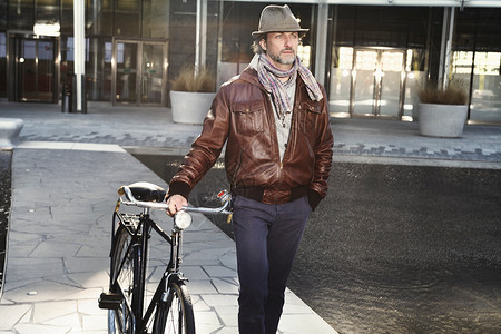 城市中扶着自行车行走的中年男子图片