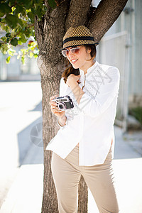 戴着太阳眼镜和帽子的成年女性拿着相机微笑图片