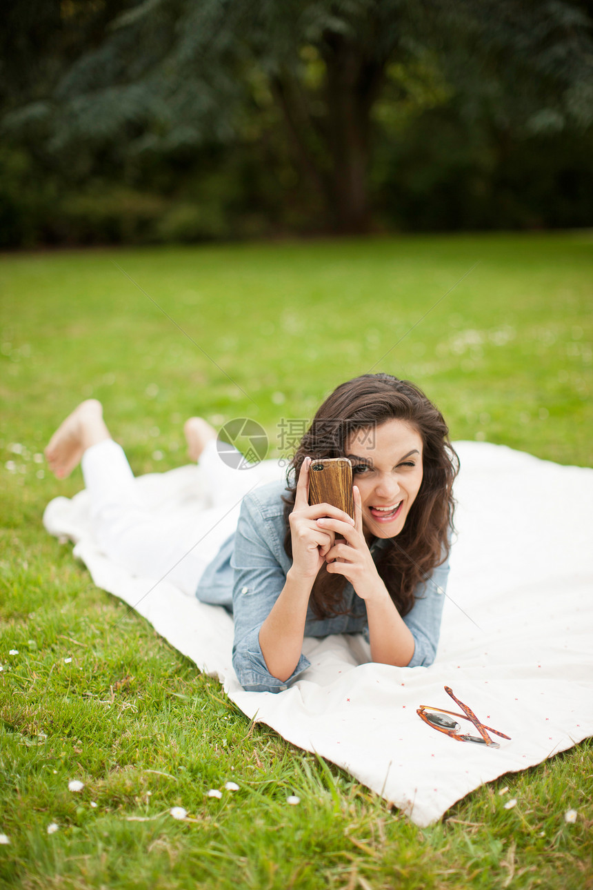 躺在公园中使用手机拍照的年轻女子图片