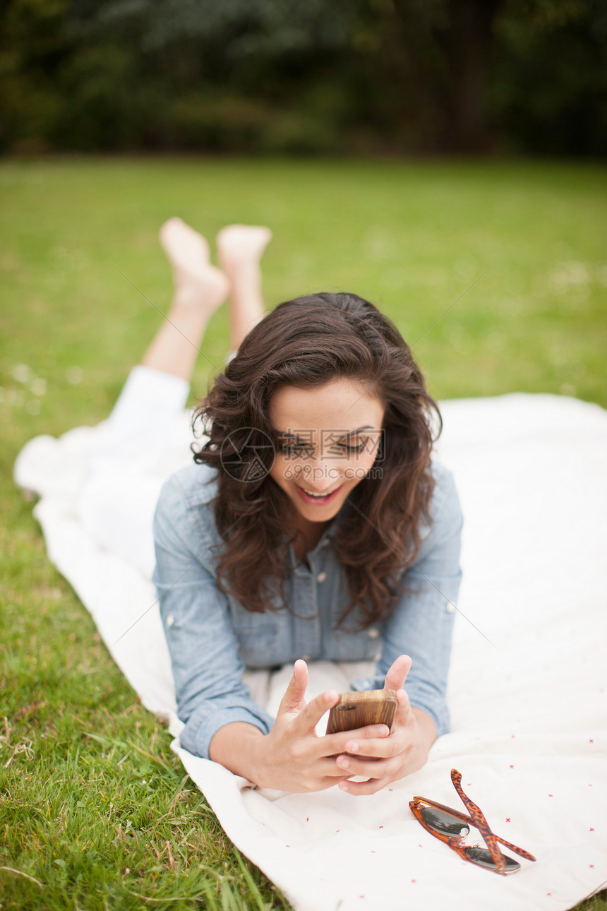 躺在公园里的年轻女人看着手机微笑图片