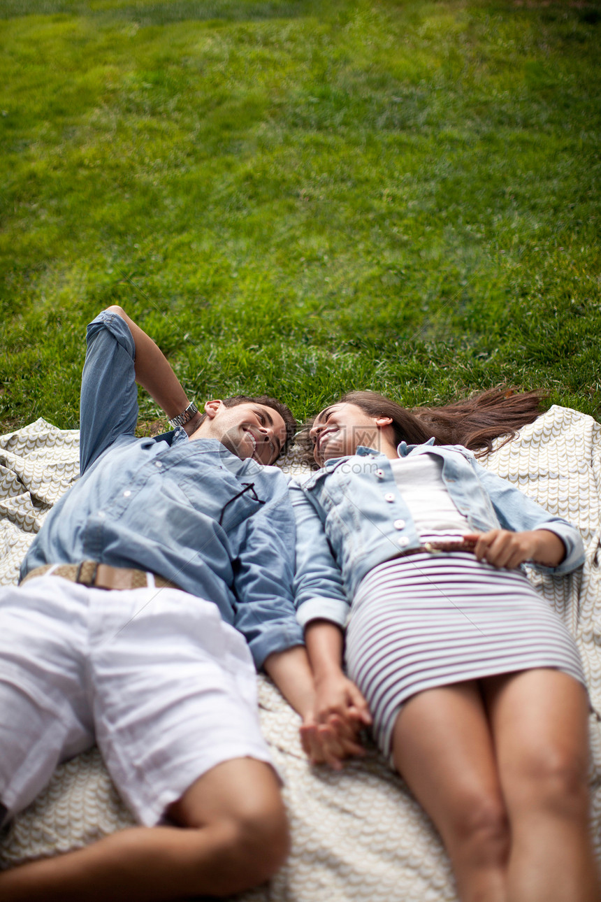 年轻夫妇躺在野餐垫上手牵手图片
