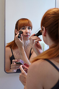 镜子前涂抹腮红的年轻女性图片
