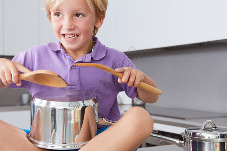 坐在厨房柜台用锅和木勺子打鼓的男孩图片