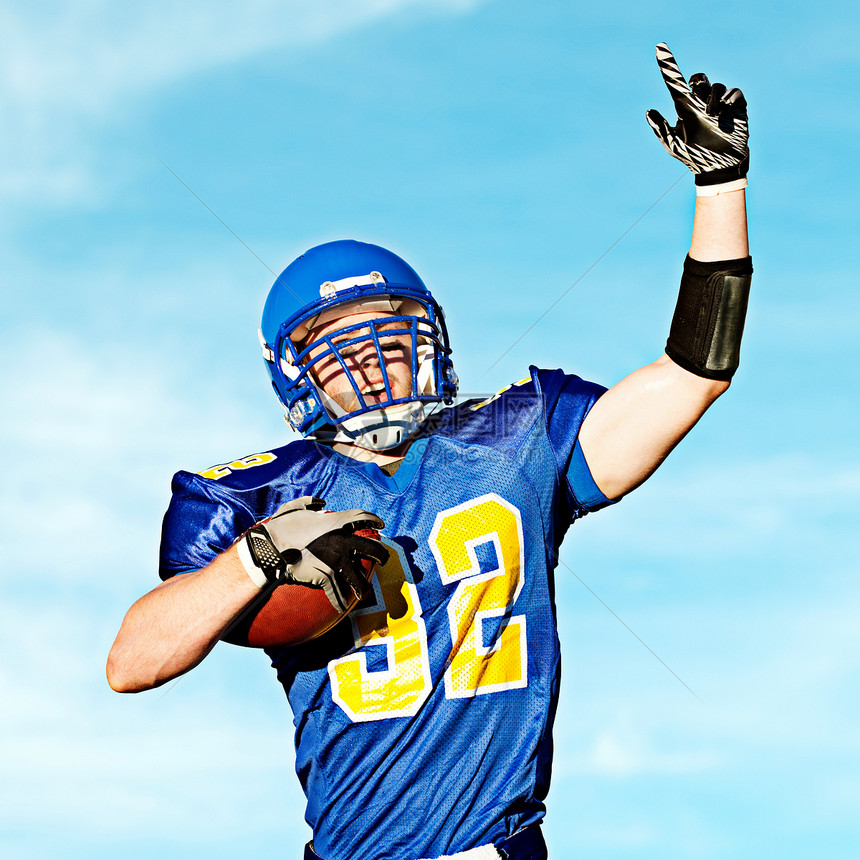 美国运动员一边抱着橄榄球一边指向天空图片