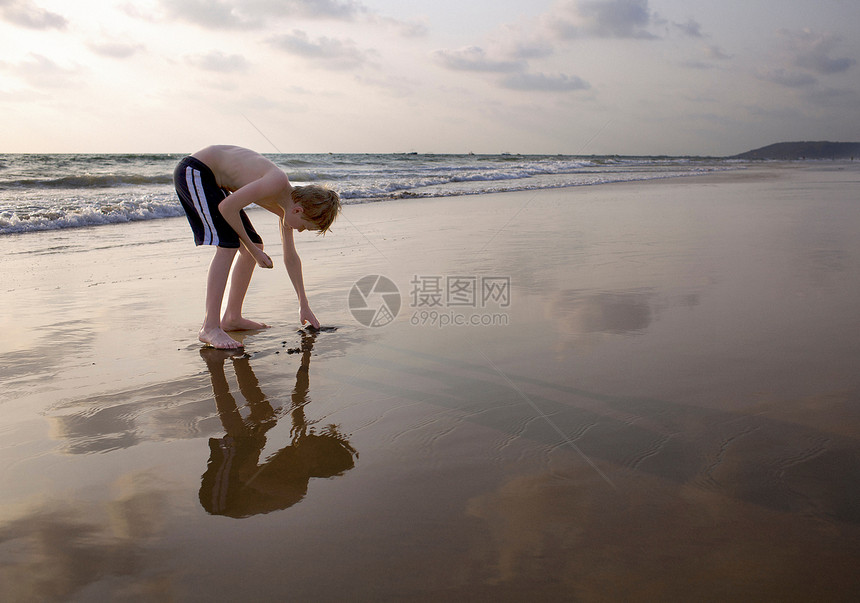 男孩在海滩上弯的触摸沙图片