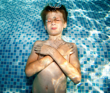 游泳池水中双手抱胸闭眼的男孩图片