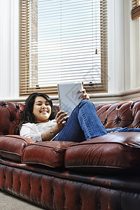 躺在沙发上的年轻女人看着数字平板电脑图片