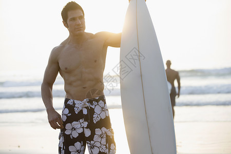 拿着冲浪板站在海滩上的男人背景图片