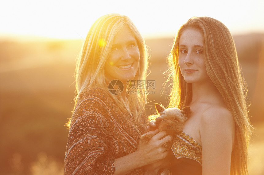 女子和朋友抱着小狗站在黄昏下图片