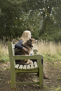 少女与狗一起坐在乡村长椅上图片