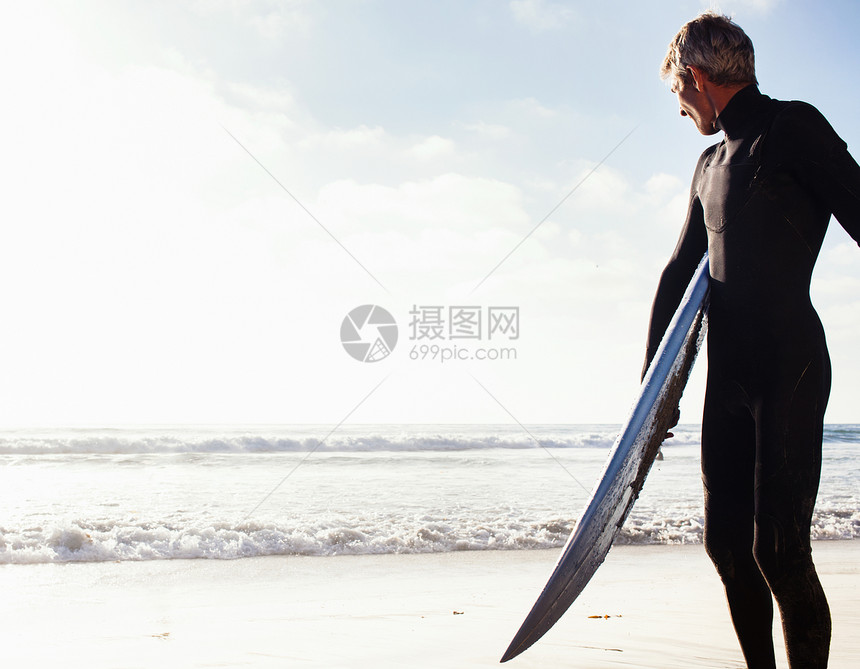 海岸上拿着冲浪板的青年男子图片