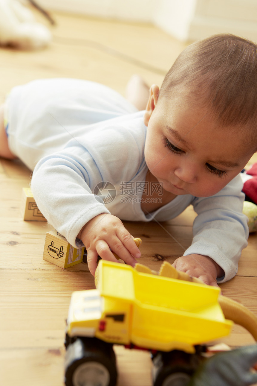 婴儿躺在地上玩前面的积木和卡车图片