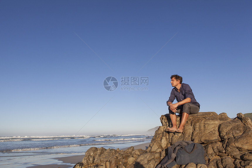 坐在海边岩石上的男人图片