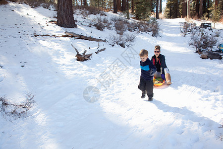 小男孩拉着外婆在雪地森林上滑行图片